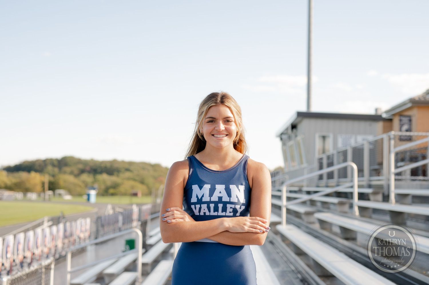 Athlete in navy Man Valley uniform poses confidently on bleachers with arms crossed.