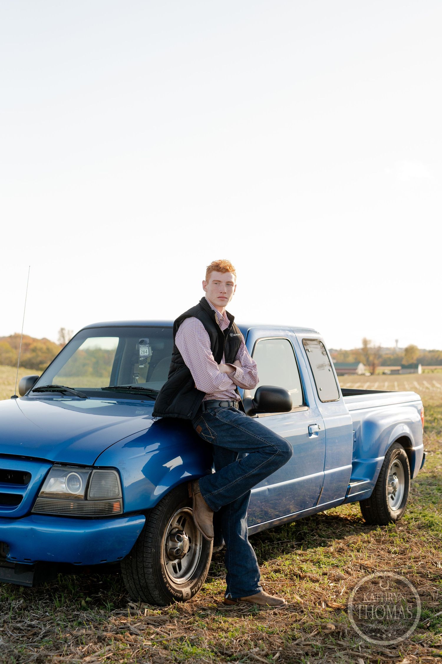 A person leaning against a blue pickup truck in a rural setting.