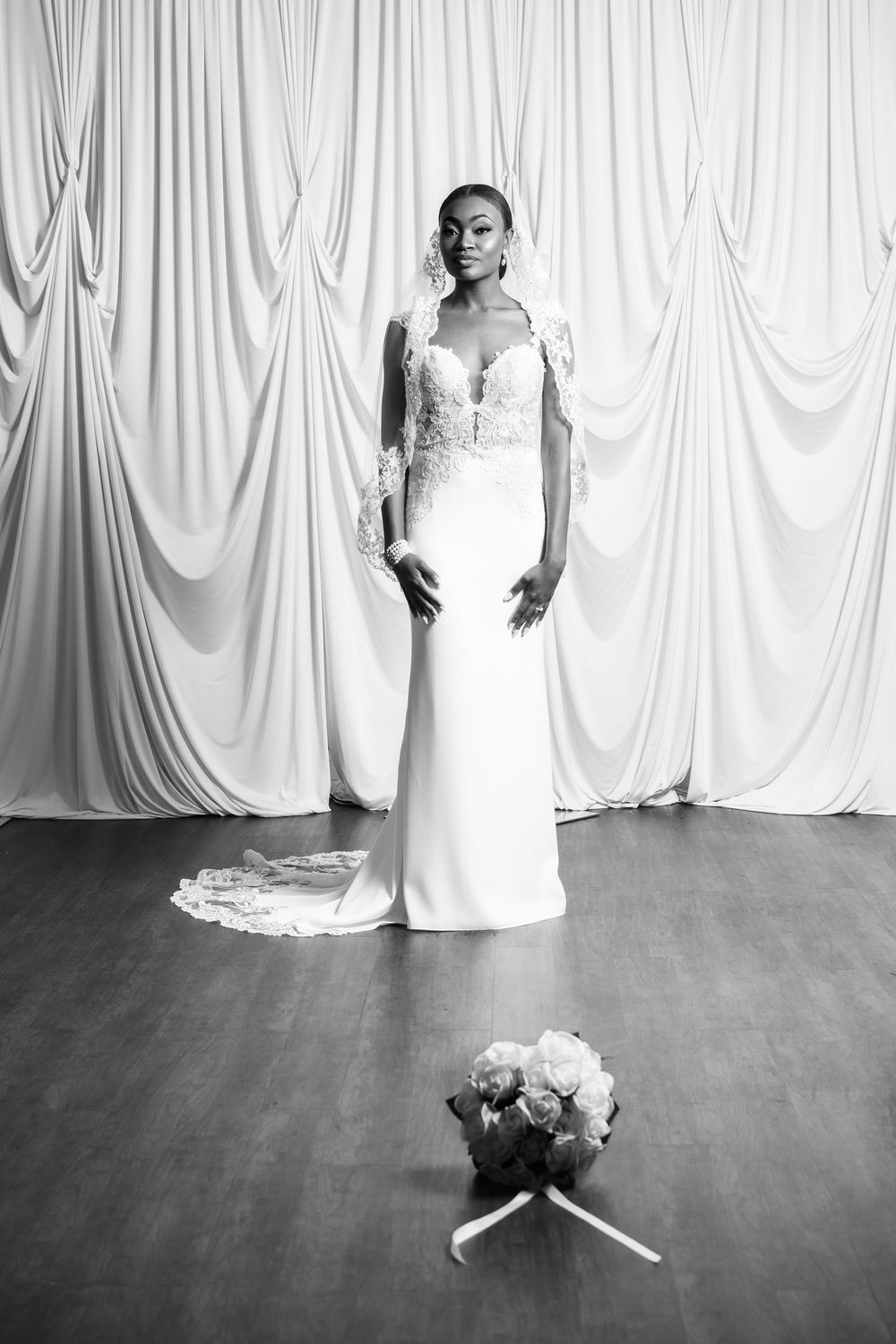 Elegant bridal portrait in front of white draped backdrop with bouquet on floor.