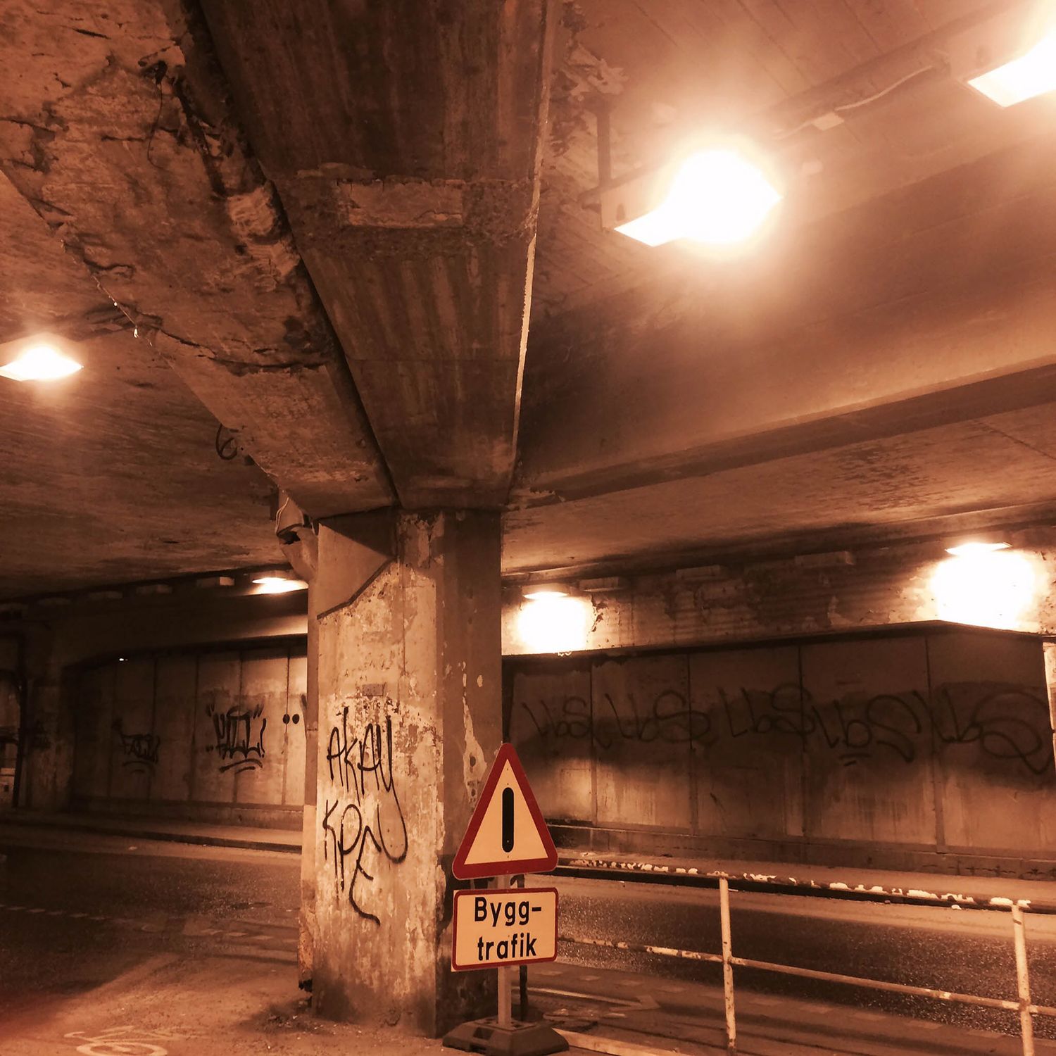 Car road, under a tunnel. Traffic sign and some graffiti tags on a pillar.