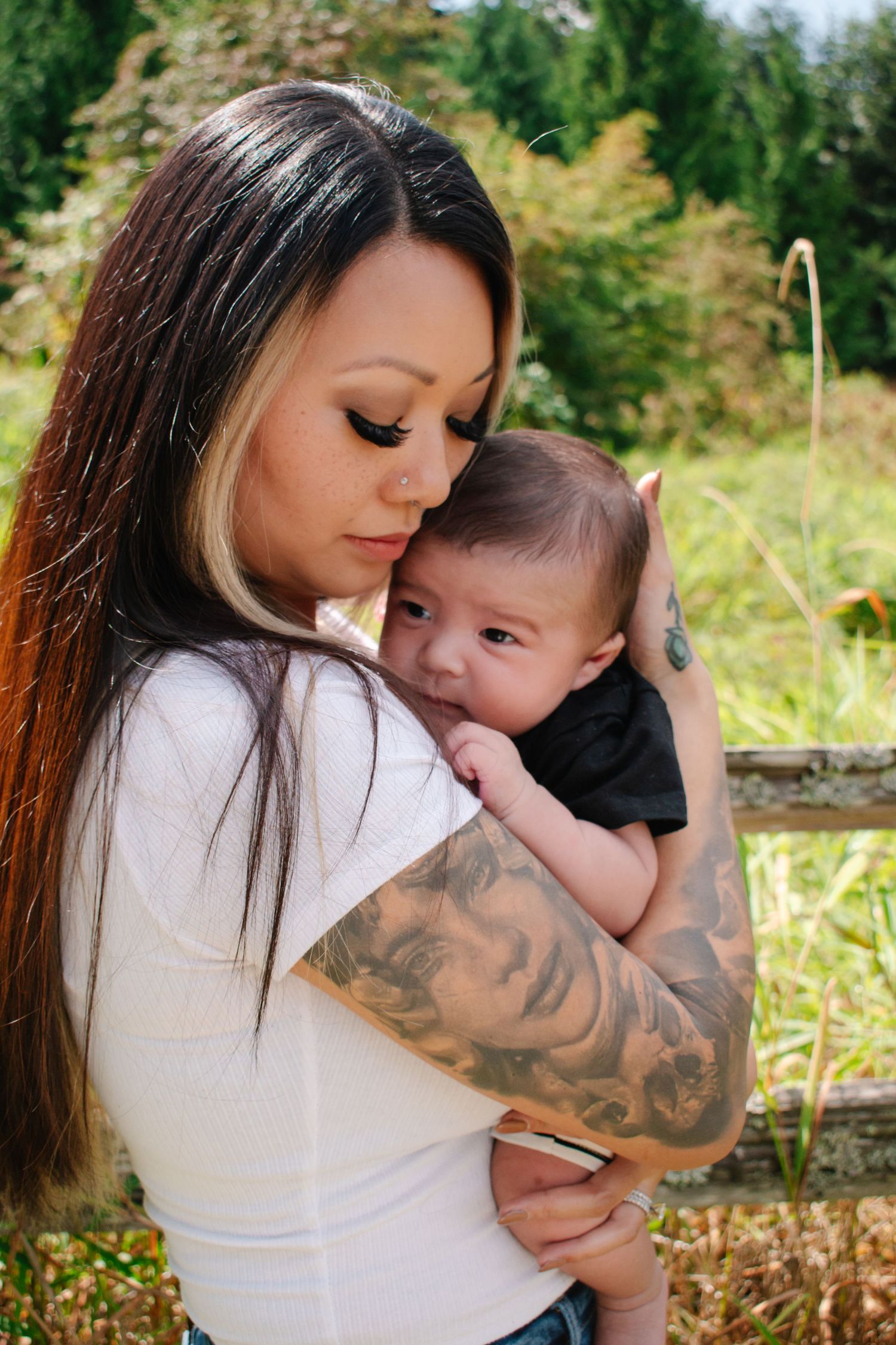 A mother in a white long-sleeved shirt holding a small baby outdoors with autumn foliage in the background. Seattle family photography.