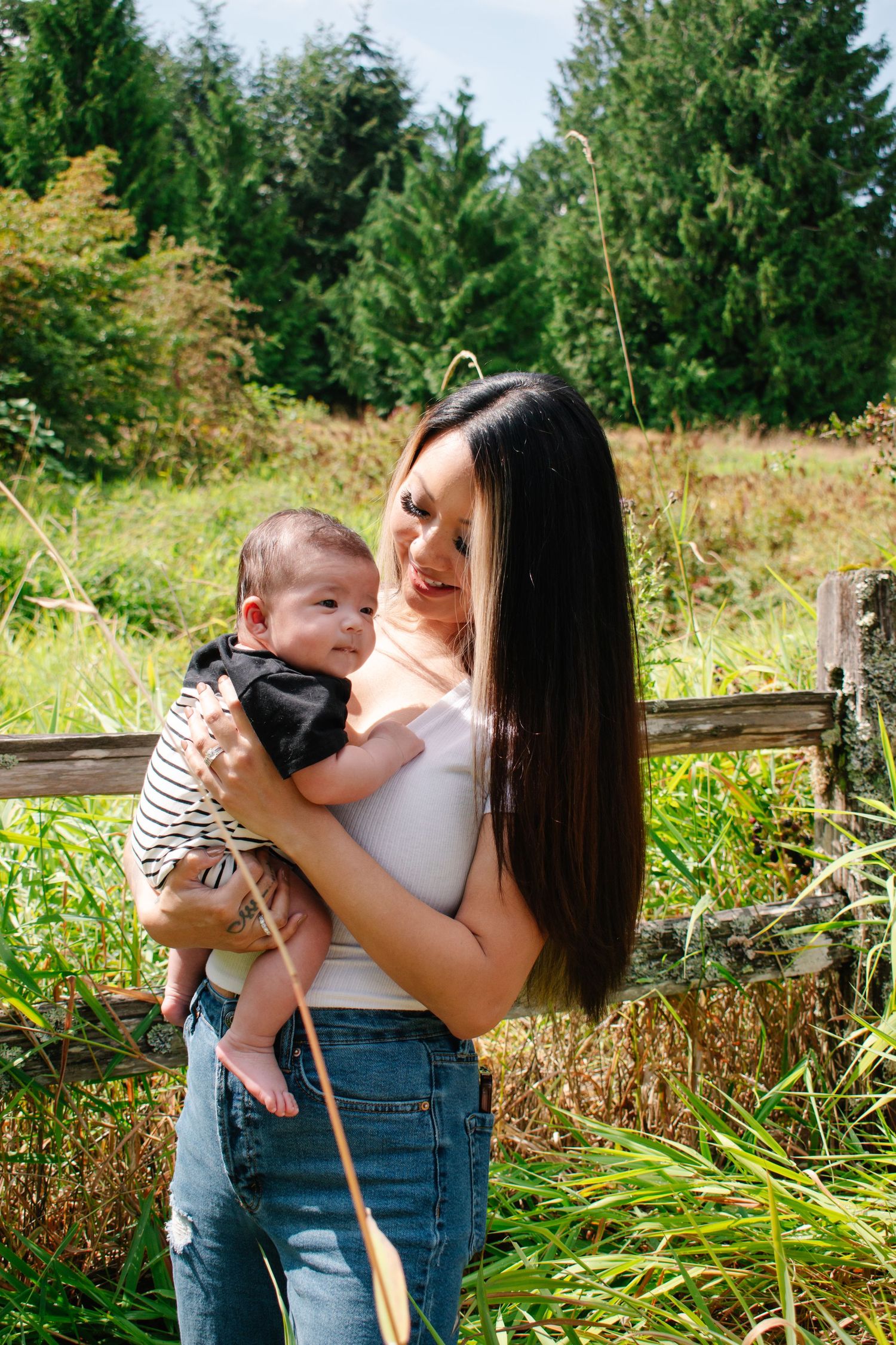 Seattle motherhood photography. Mother and son share a tender moment outdoors among lush evergreen trees and wild grasses on a sunny day.