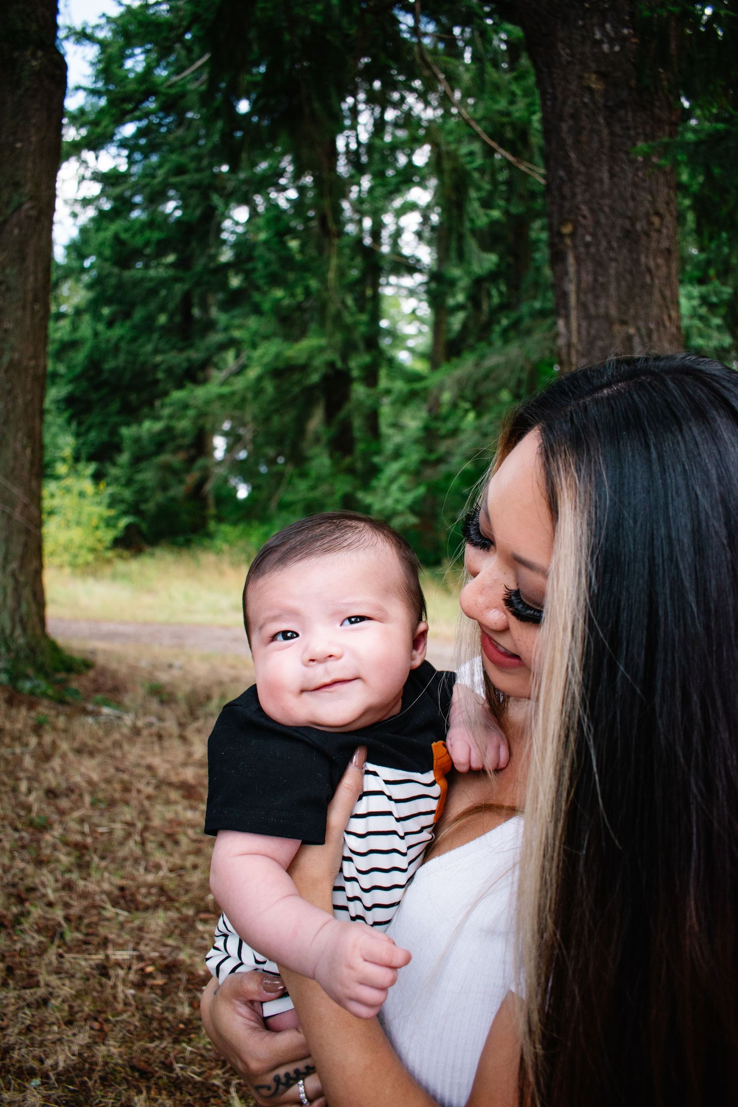 Seattle motherhood photography. A sweet moment captured in a forest setting as a mother holds her smiling baby wearing black and stripes.