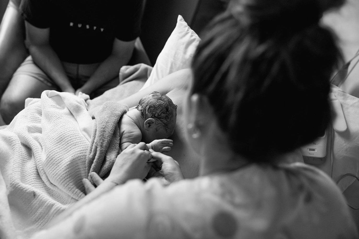 A newborn baby rests on his mothers chest while the midwife checks his stats