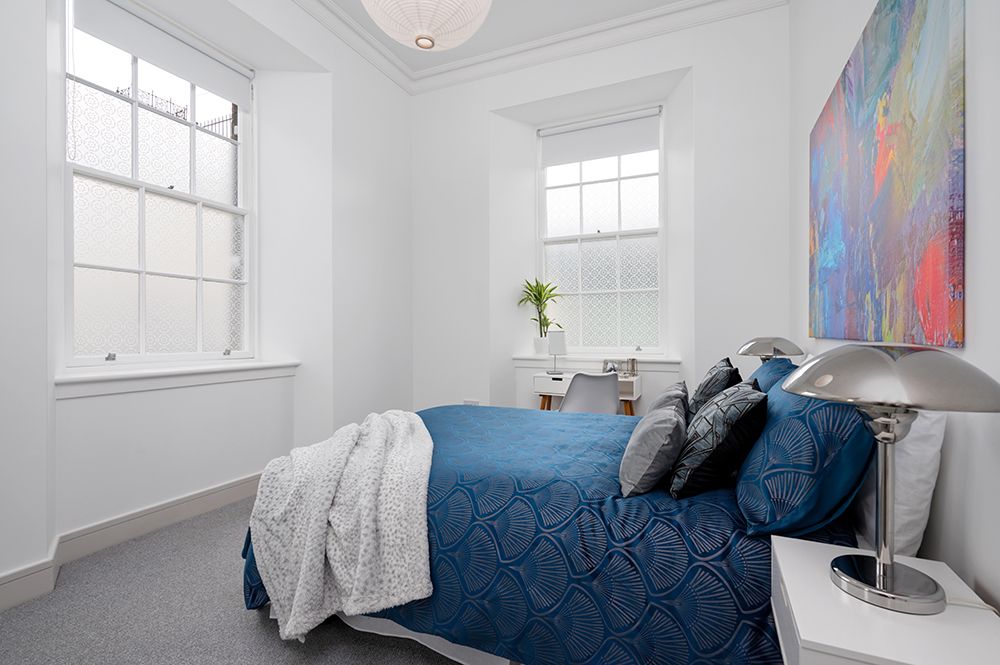 White bedroom with double bed and blue accent colours. Modern apartment building photographed for builder in falkirk