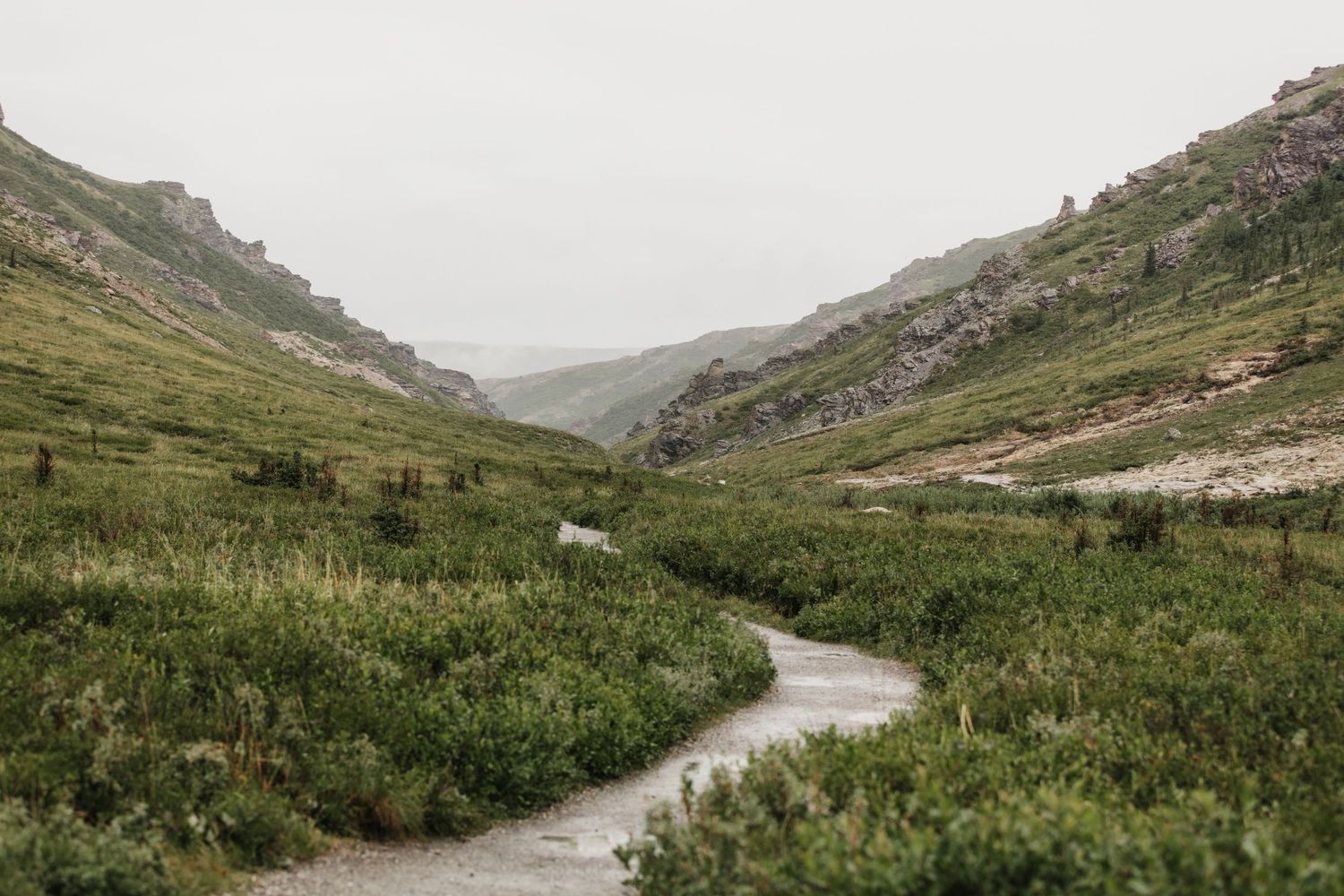 Photographer in yellow jacket crouches to capture mountain landscape.