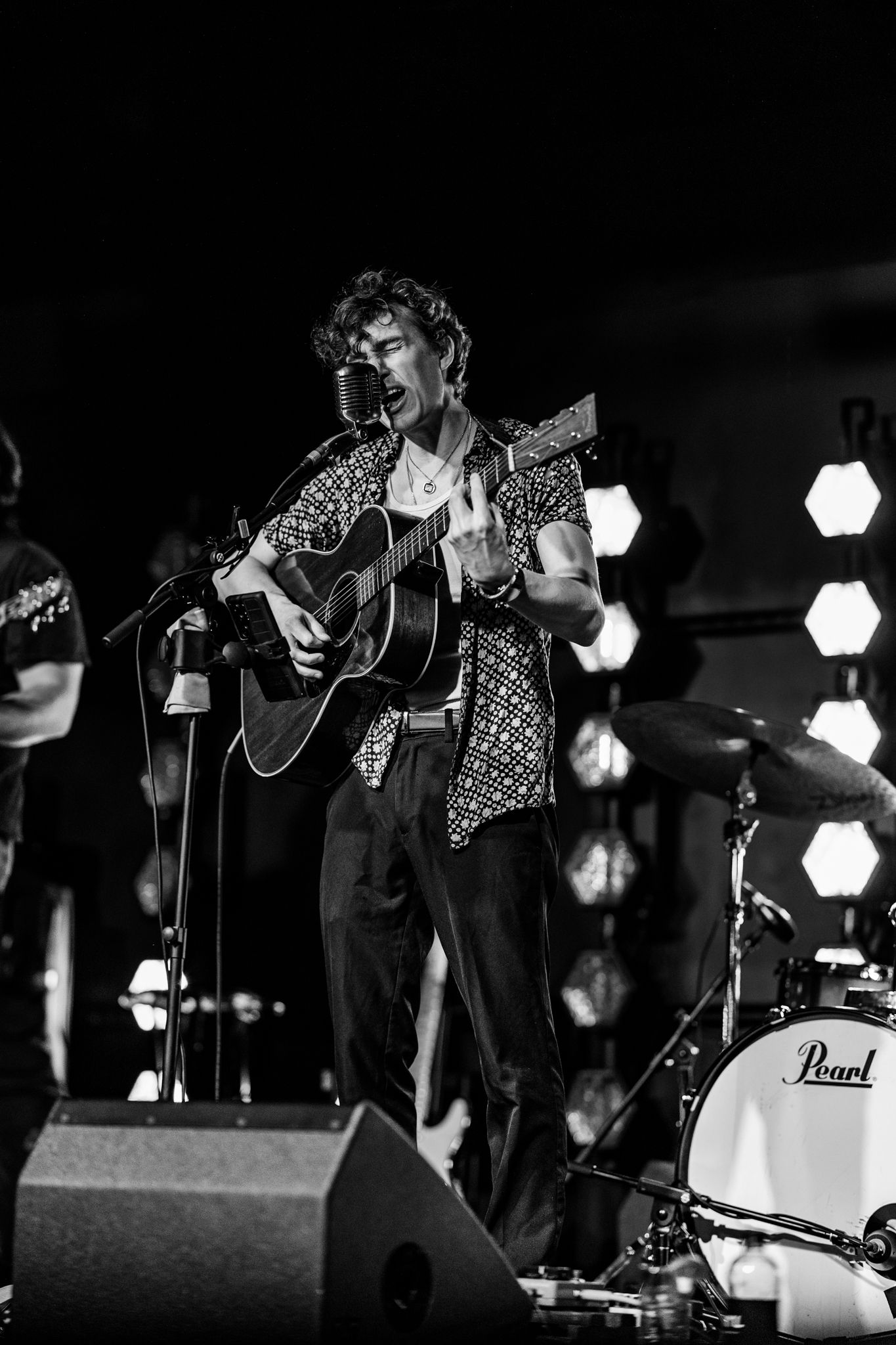 Musician performing on acoustic guitar in black and white with hexagonal stage lights.