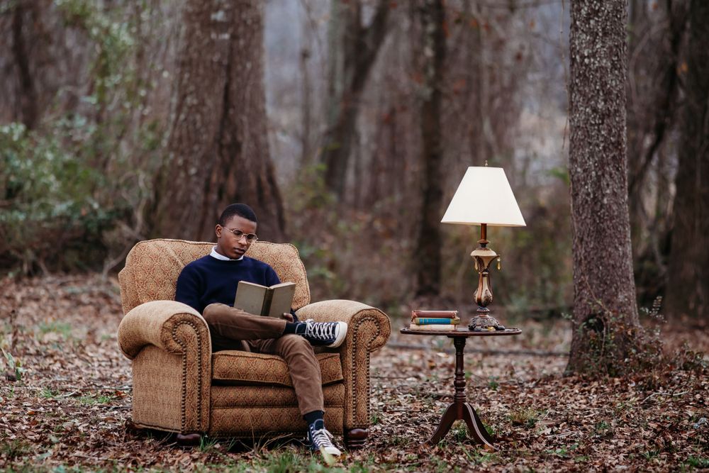 An armchair and reading lamp set up outdoors in a wooded setting creates a cozy reading nook.