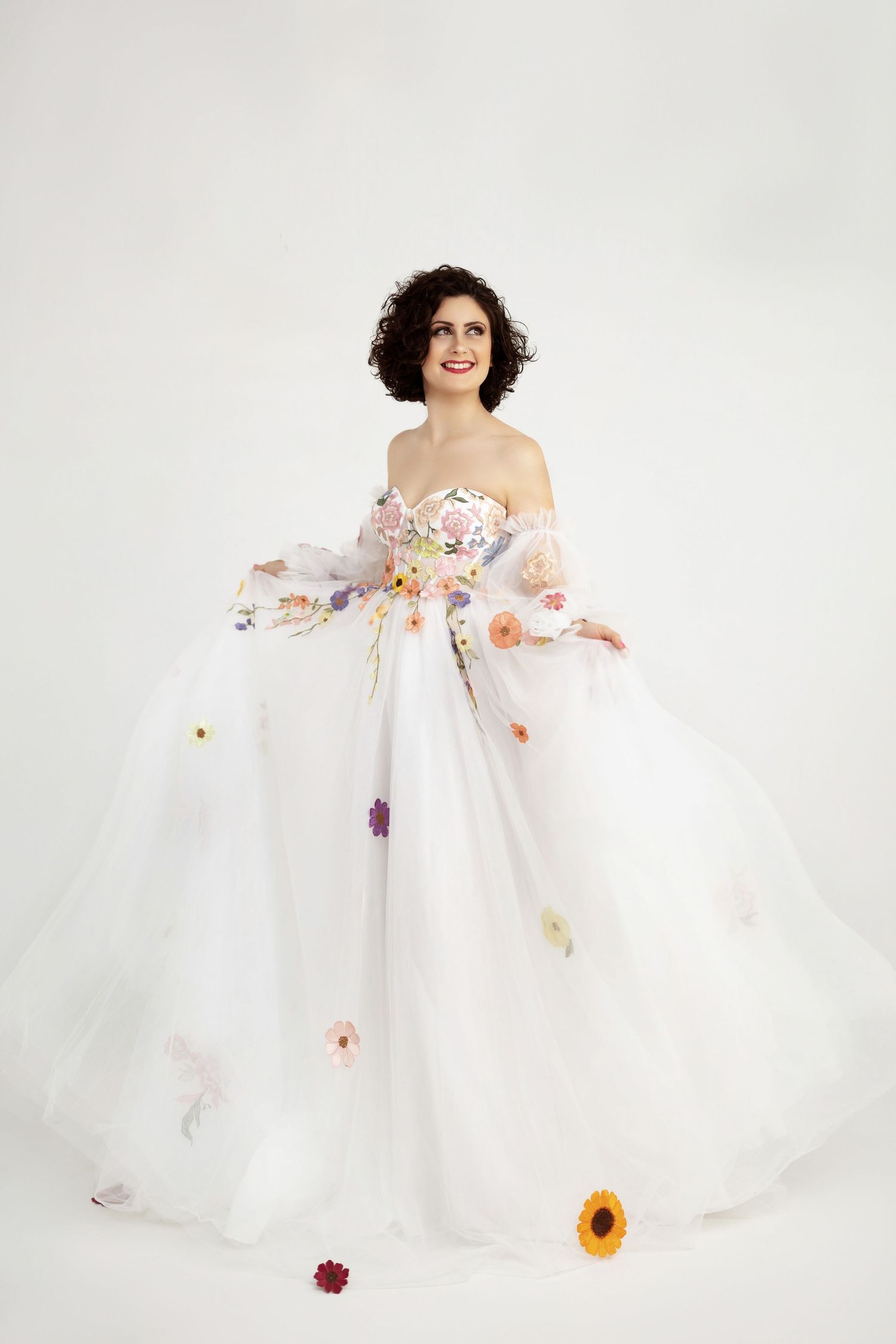 A flowing white wedding gown with delicate floral appliques adorns a figure against a bright white backdrop.