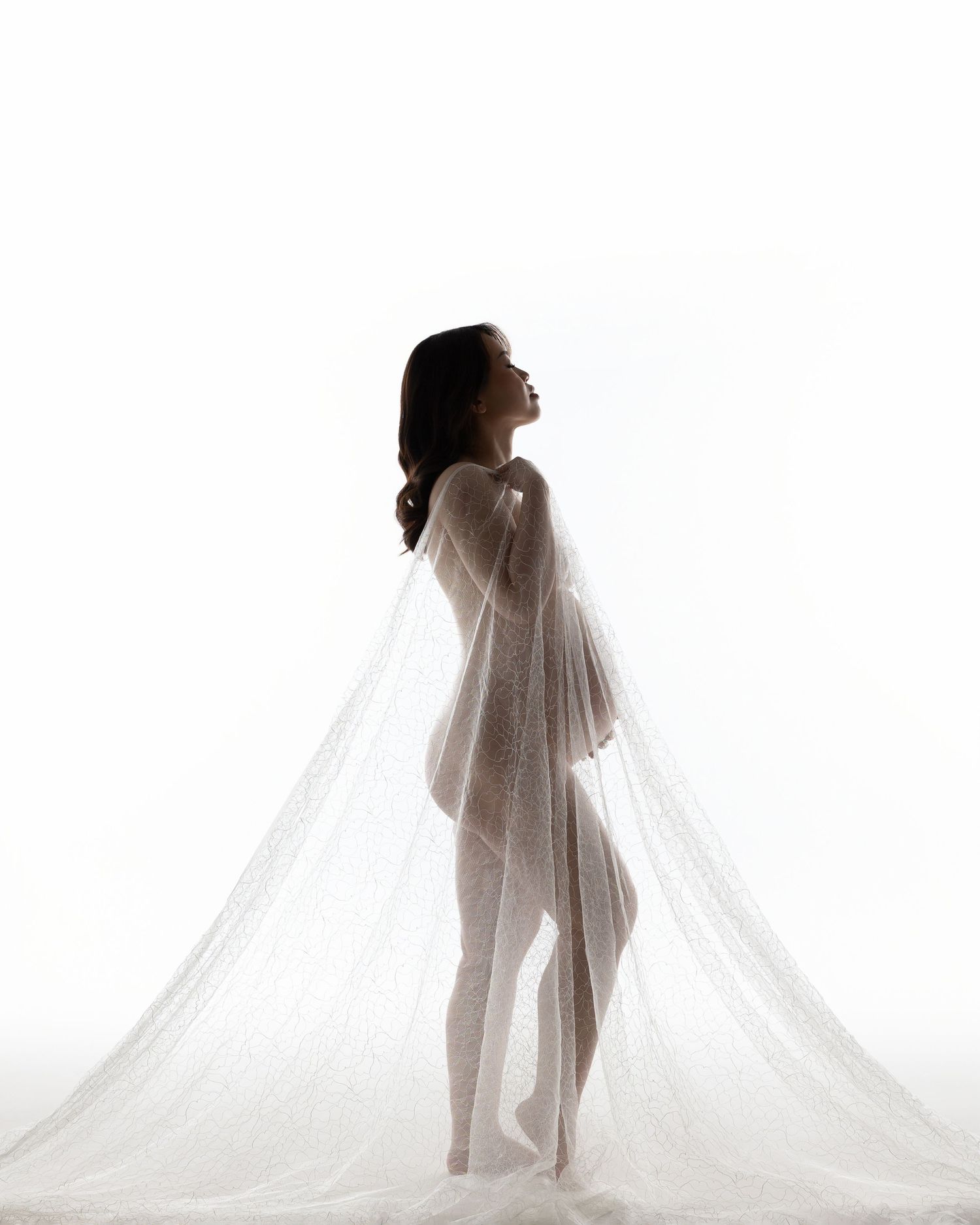 Artistic silhouette of a person draped in flowing sheer fabric against a white background in a graceful pose.