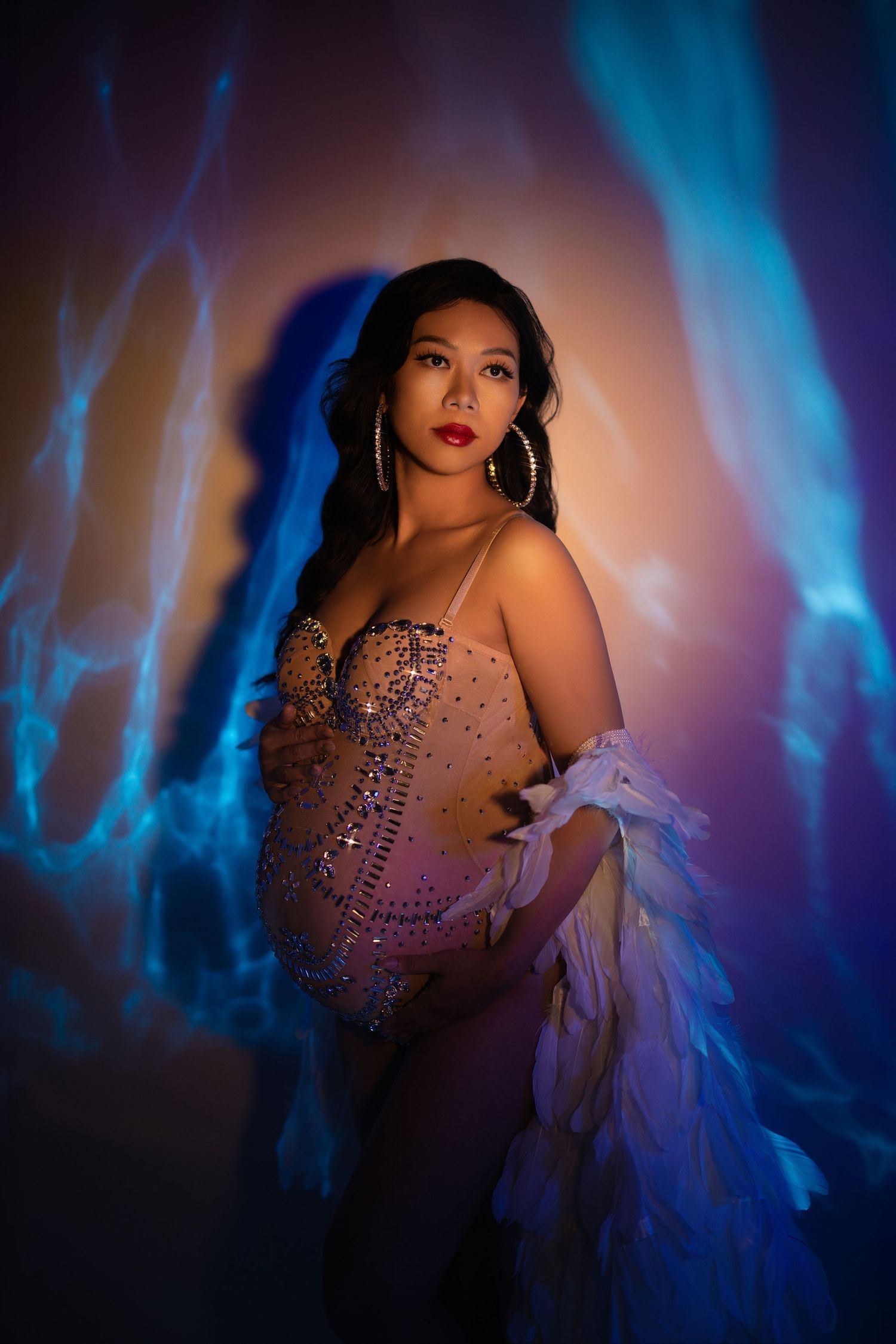 Glamorous portrait with sparkly corset and white feathers against blue and orange atmospheric lighting effects.