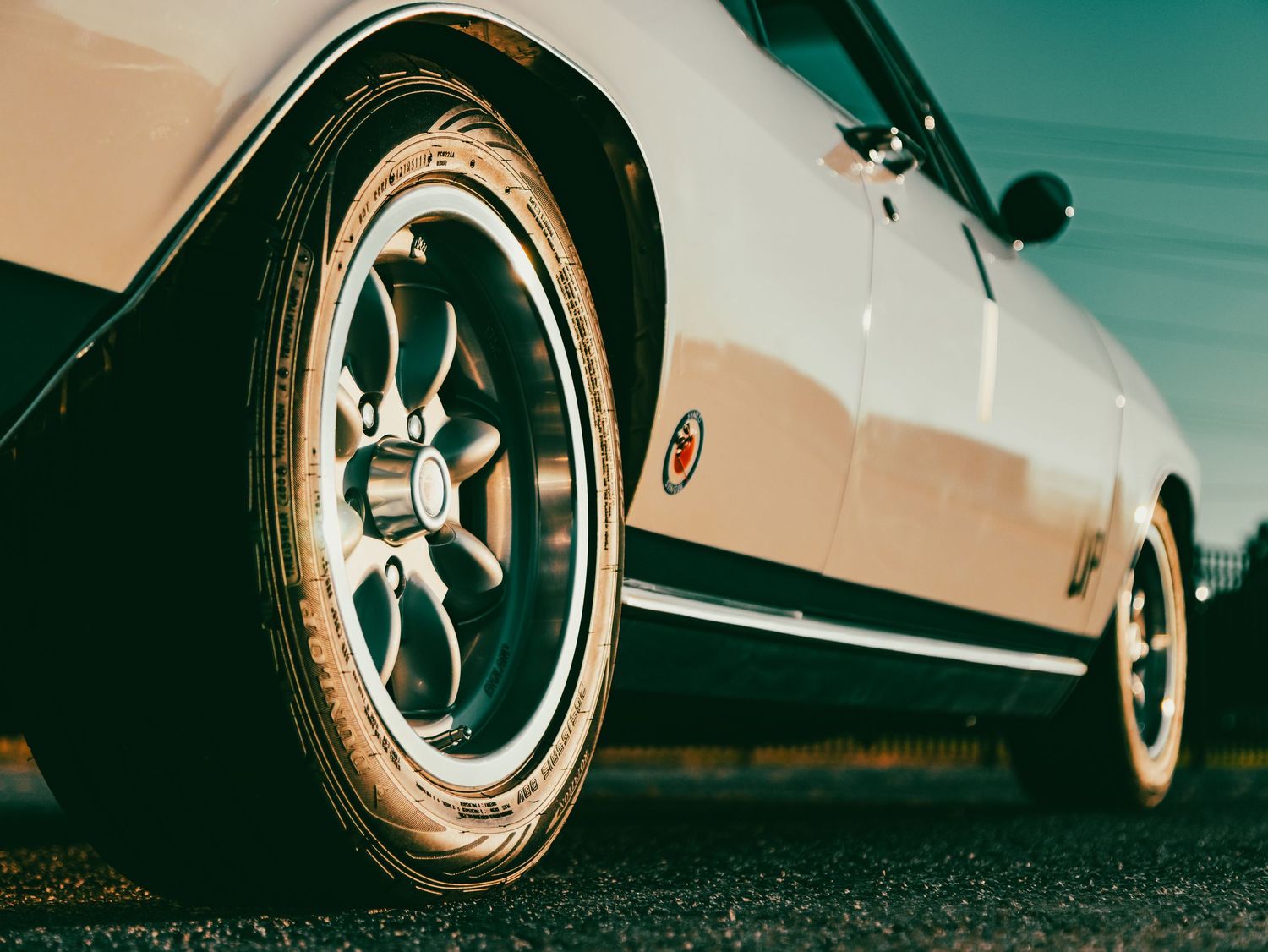 Close-up of a vintage chrome wheel and tire on a classic car against blurred background.
