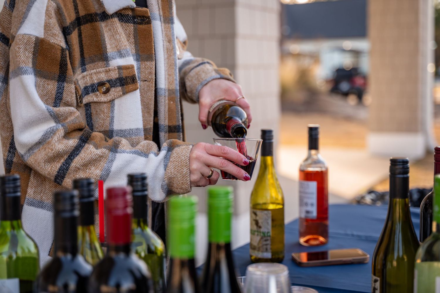 Hands opening wine bottle among collection of various wine bottles on table.