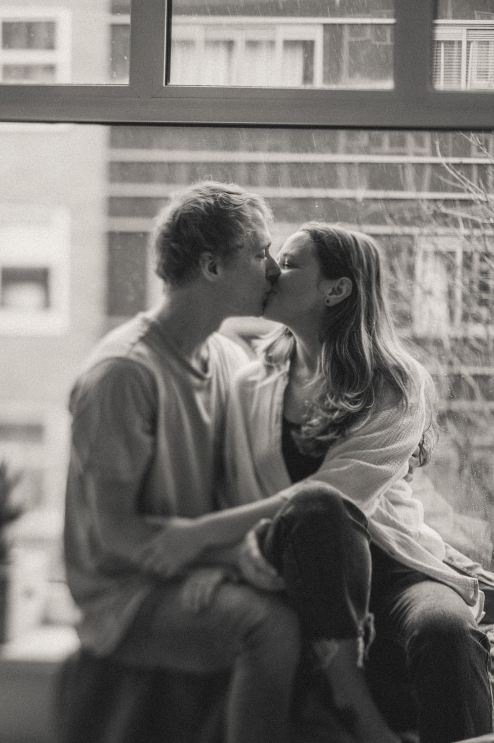 Black and white photo of a couple sharing a tender moment by a window.