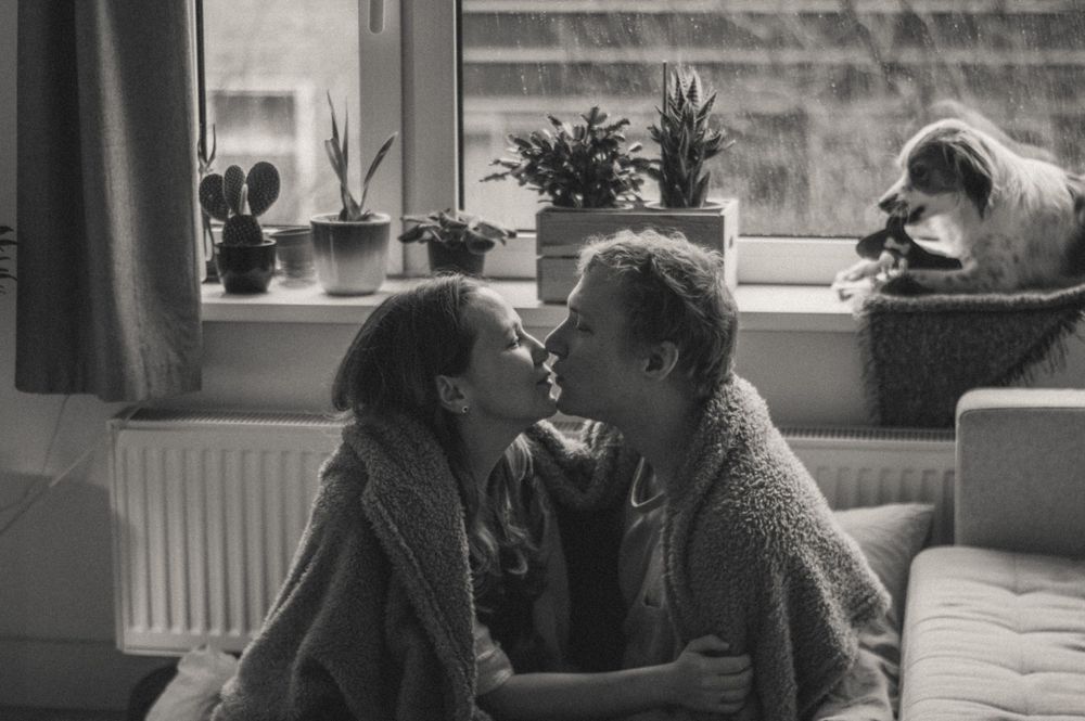 Couple lounging together on a couch near large windows in an apartment.