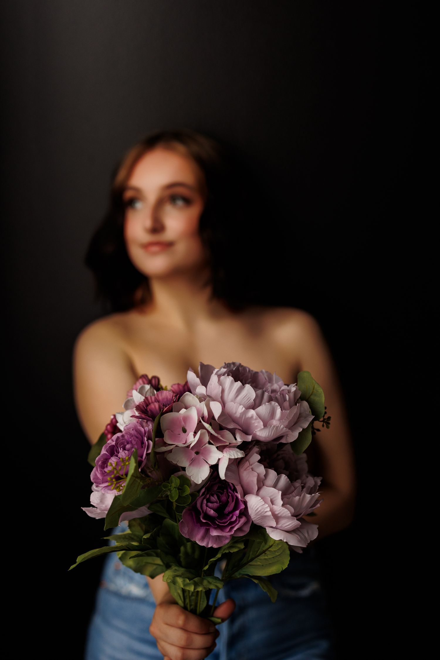 Ethereal maternity portrait holding greenery with moody lighting.