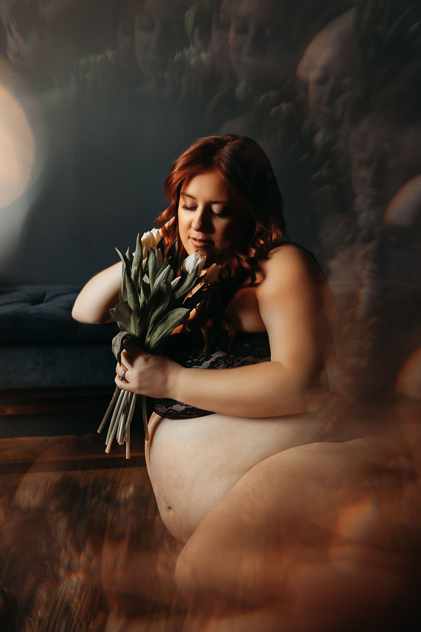 Ethereal maternity portrait holding greenery with moody lighting.