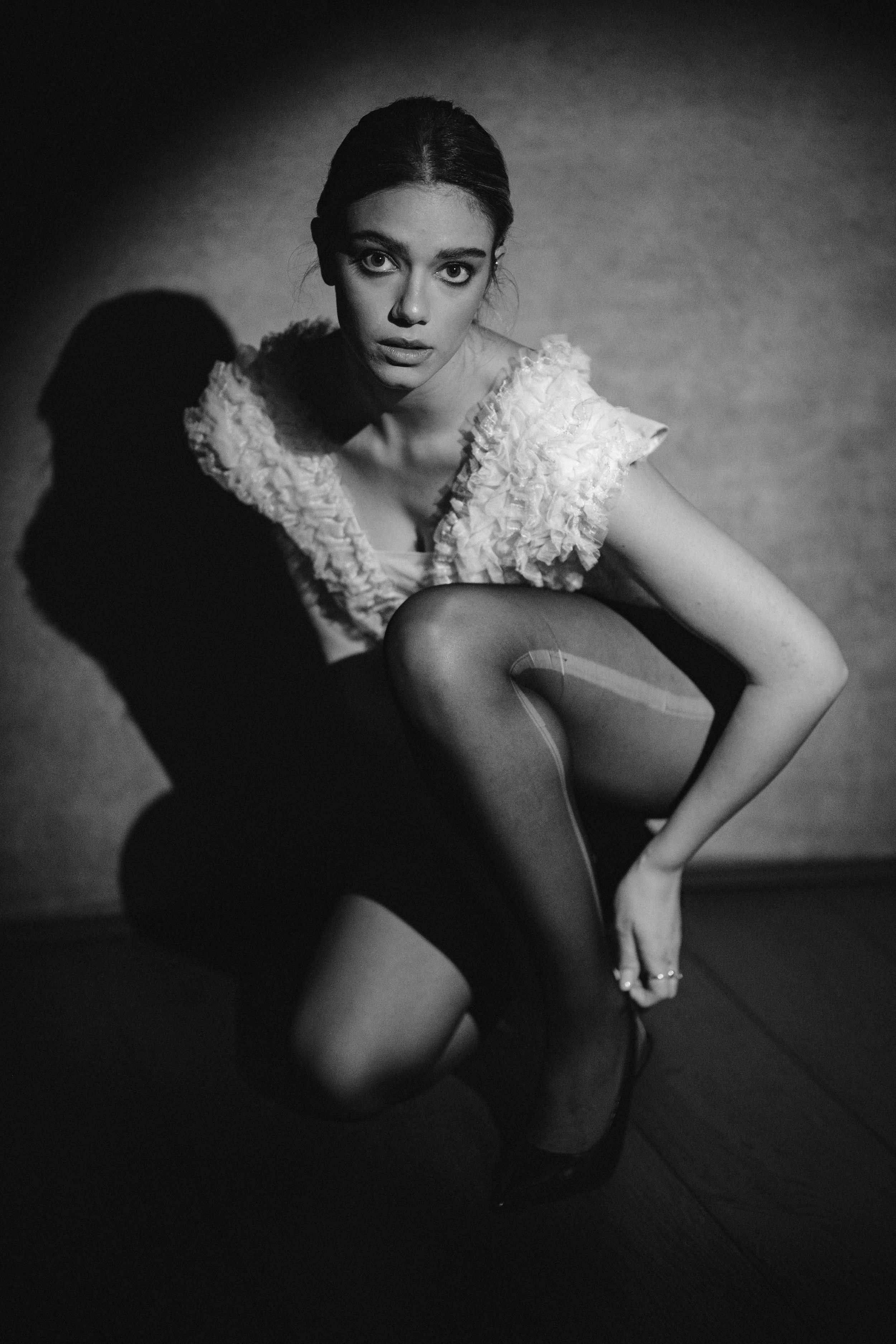 Fashion portrait in black and white showing crouching pose and textured white garment.