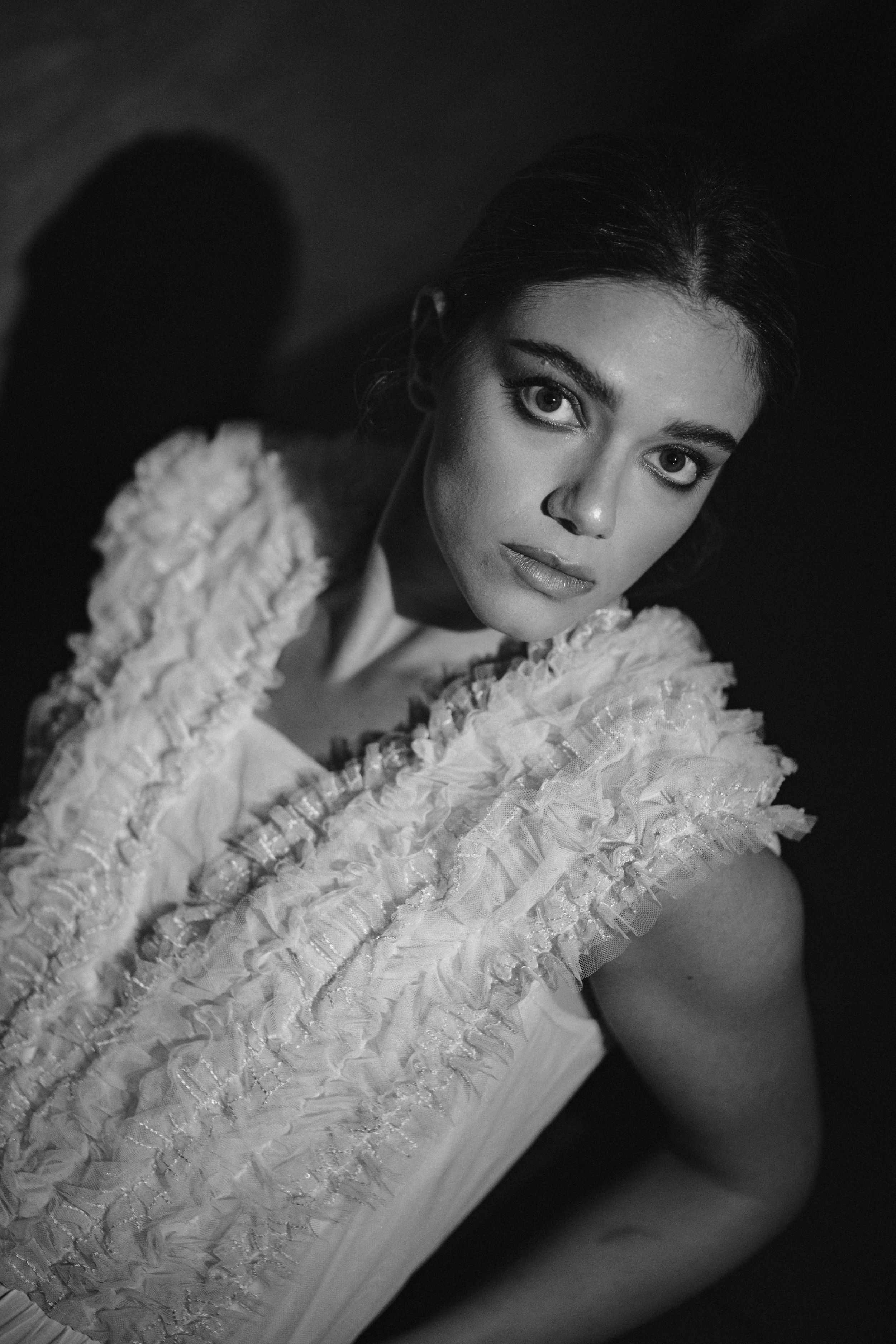 Close-up fashion portrait featuring textured white top with dramatic monochrome lighting.