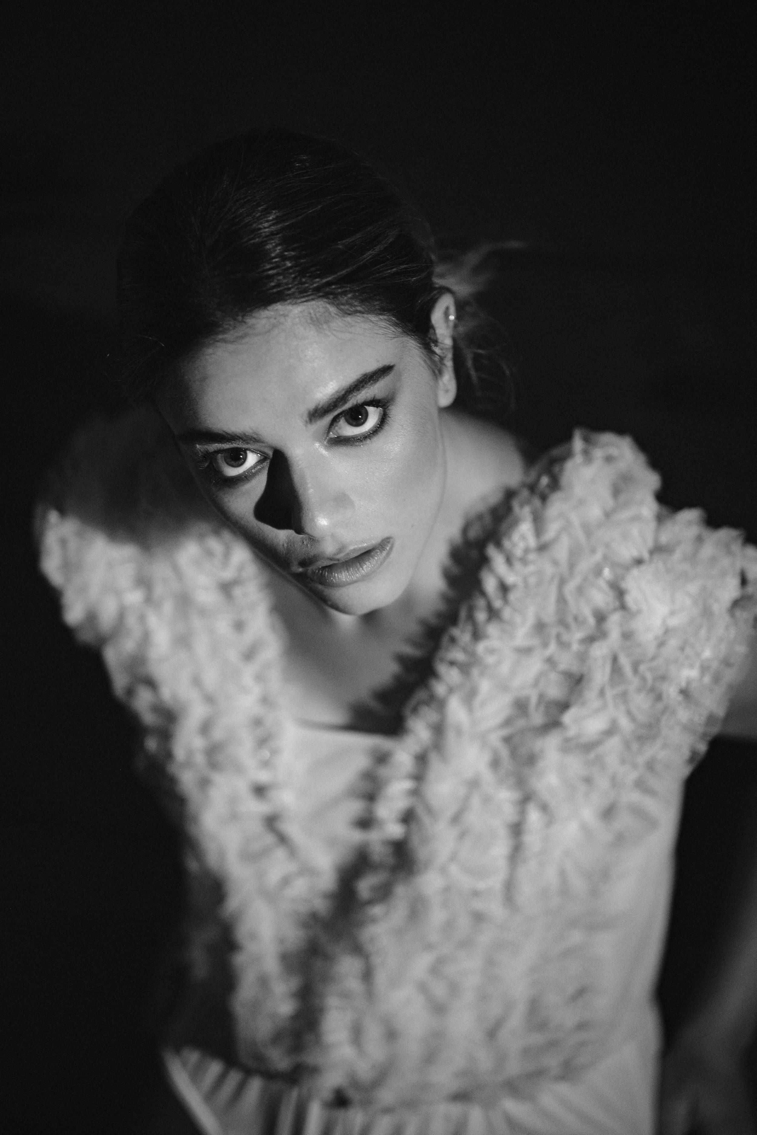 Moody black and white close-up portrait highlighting textured white garment and shadows.
