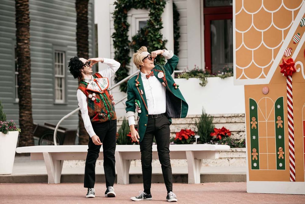 Street performers in holiday attire pose playfully in front of a gingerbread-themed post office display.