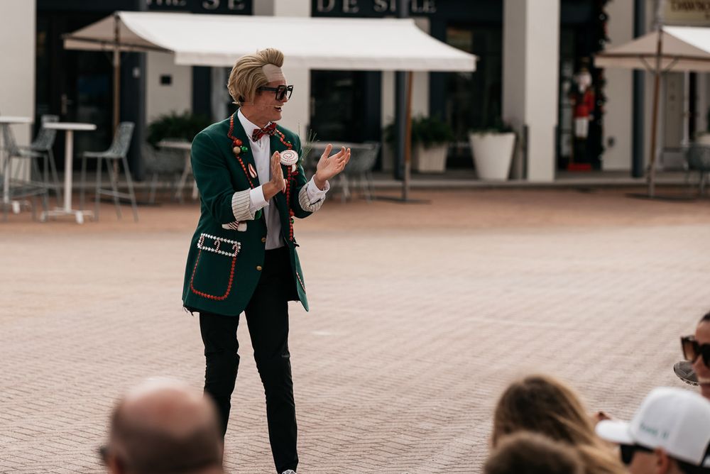 Performer in green suit jacket presents to outdoor audience during daytime show.