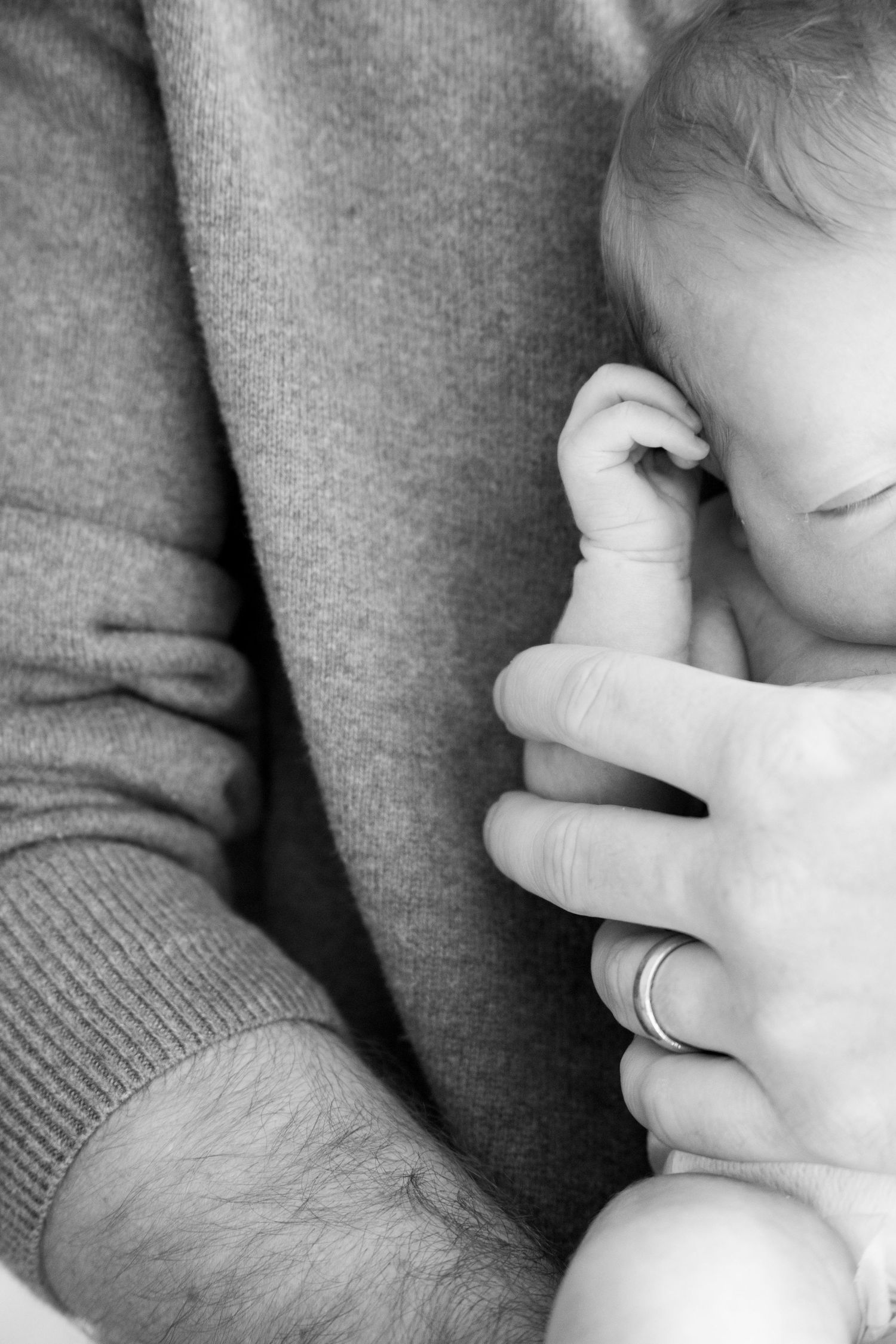 Close-up black and white image of baby's hand resting against parent wearing grey sweater.