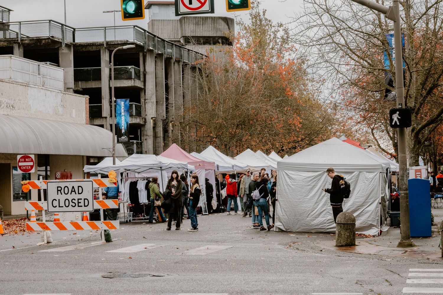 White tents and vendors line an urban street with construction barriers and pedestrians walking by.