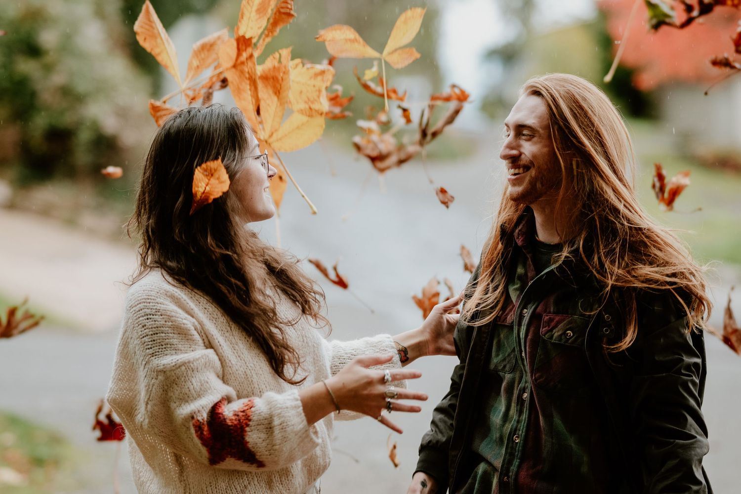 Two friends playing with falling autumn leaves while laughing together outdoors.