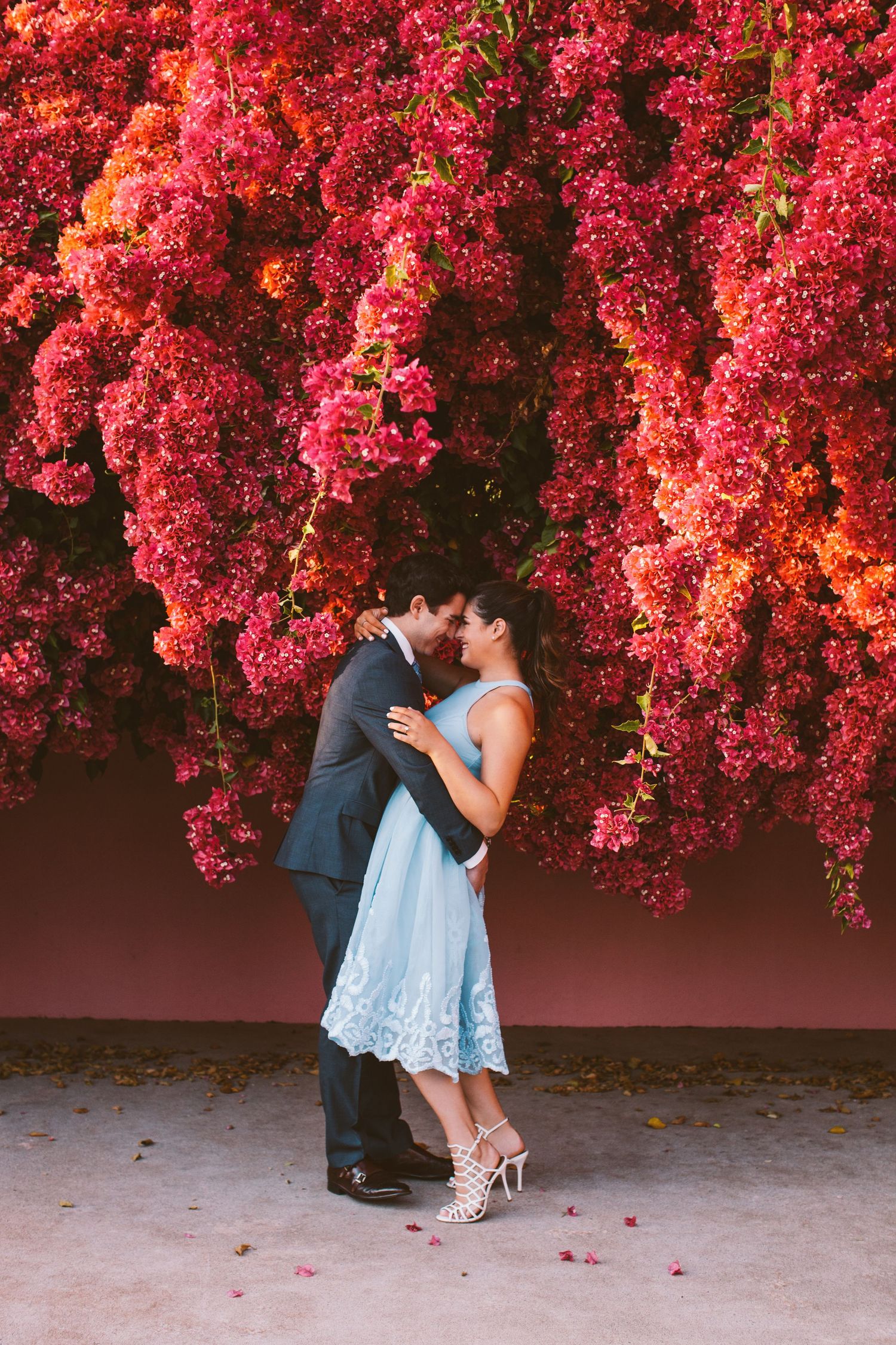 Couple holding hands while walking by pink building with vintage balcony.