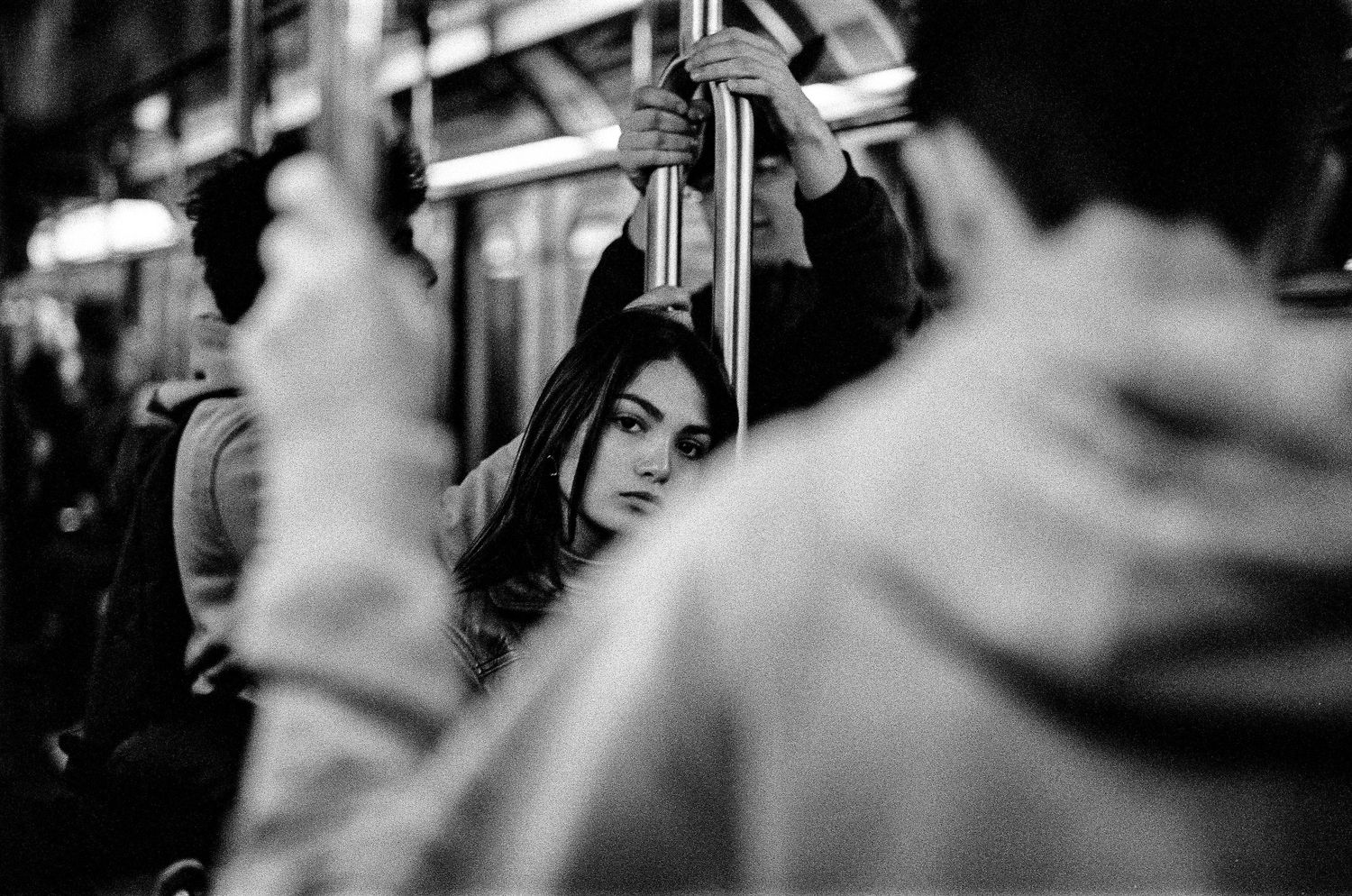 Black and white photo of commuters on public transit with someone holding onto a pole.