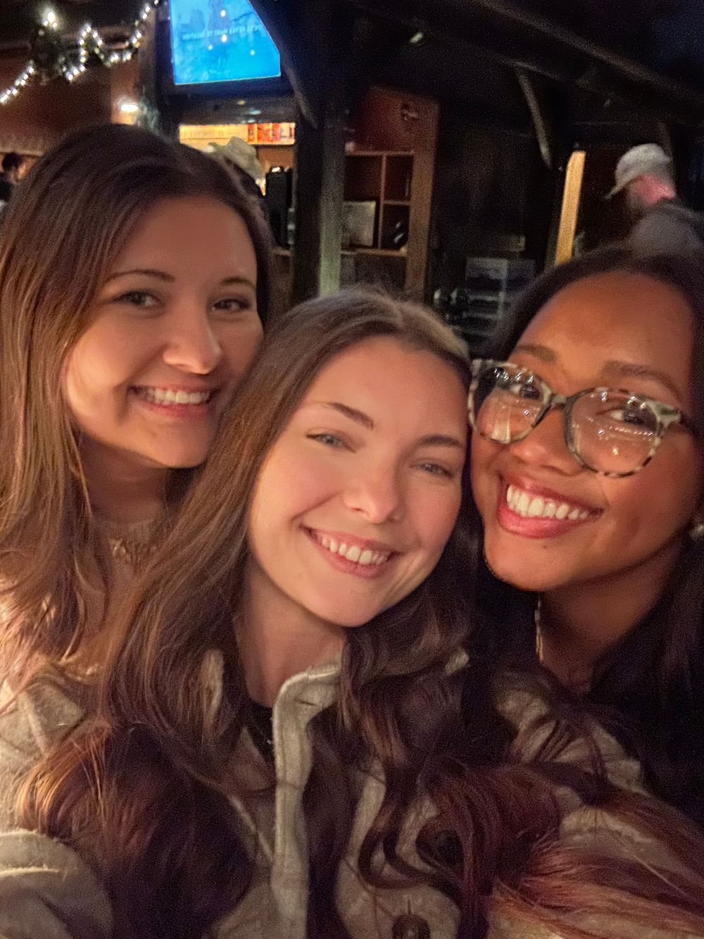 Three friends taking a cozy selfie at a dimly lit bar or restaurant.