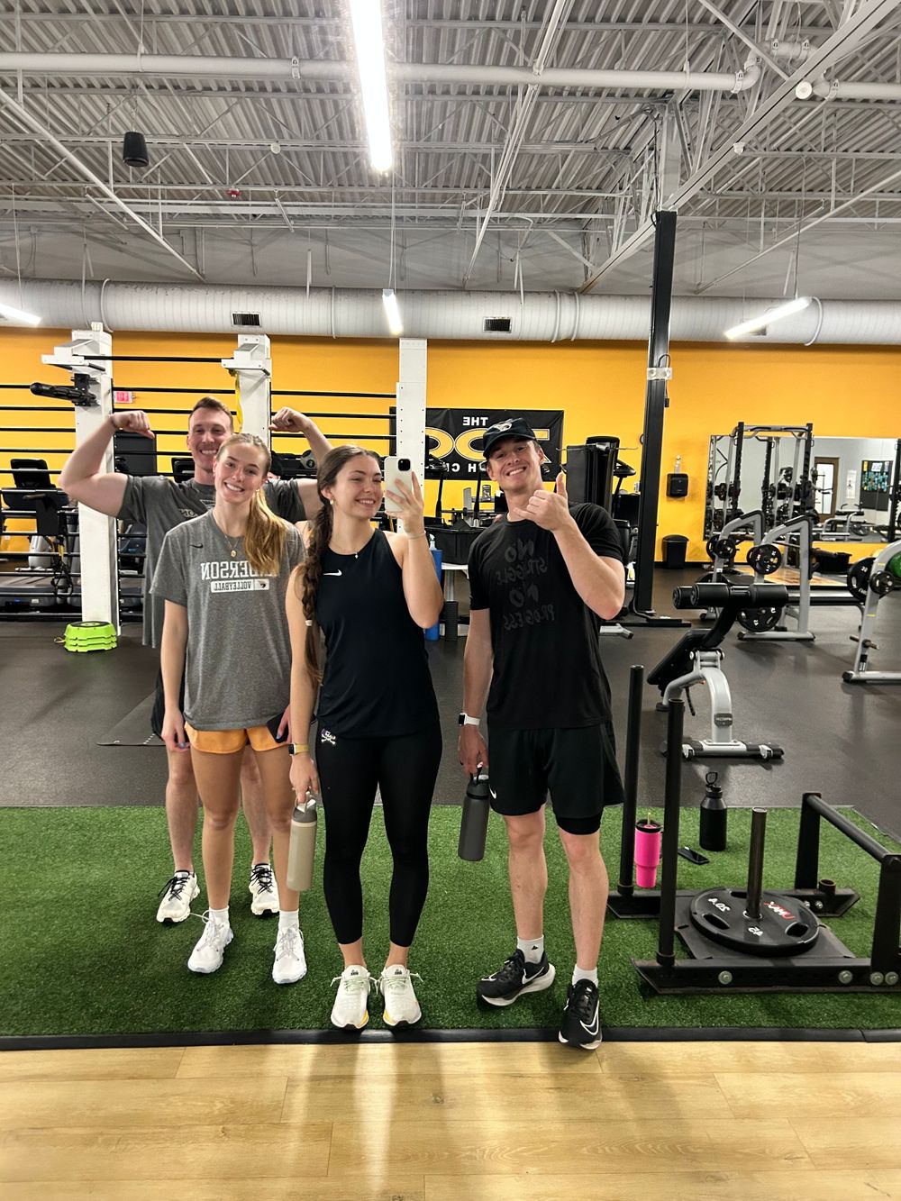 Three people holding water bottles and posing together at a gym.
