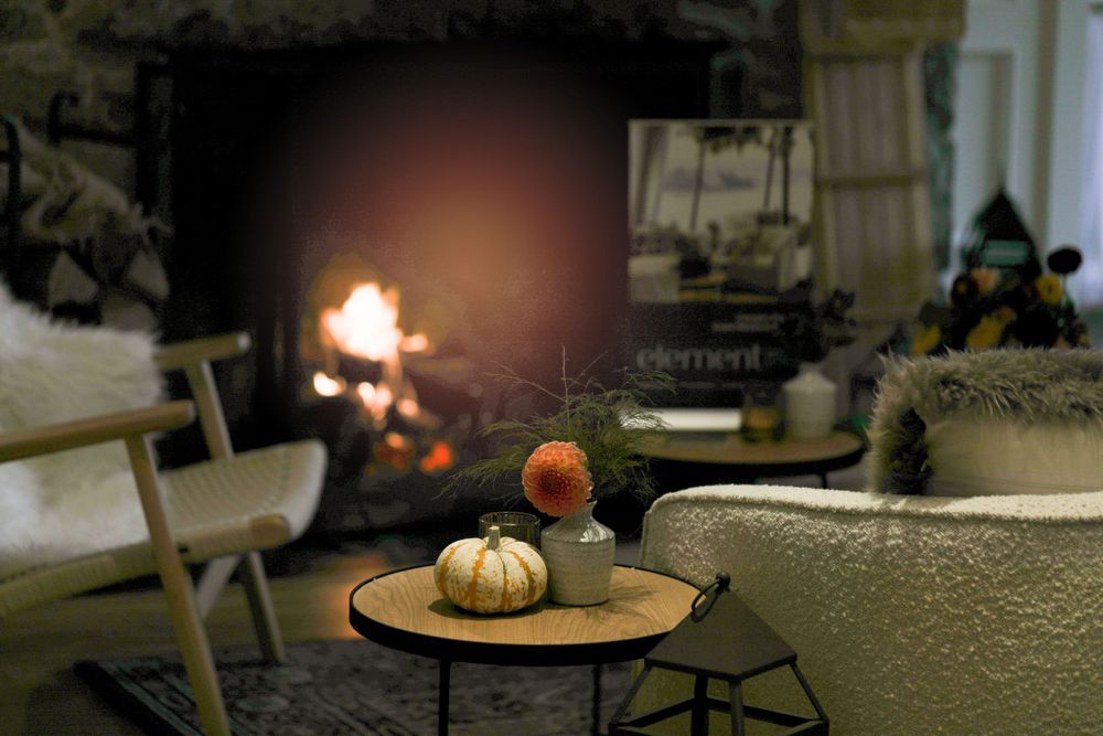 Cozy autumn scene with pumpkins on a table near glowing fireplace.