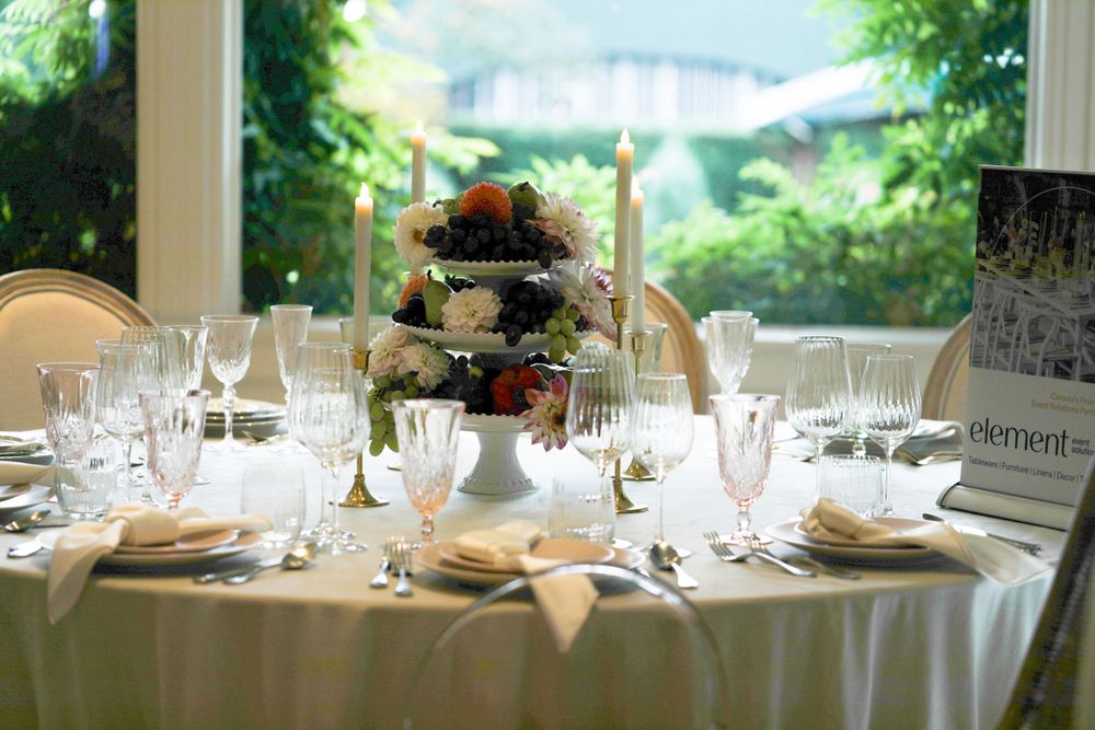 Formal dining table set with crystal glasses and tiered floral centerpiece overlooking garden view.