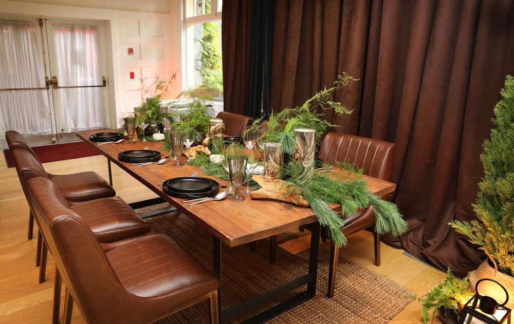 Rustic dining room with leather chairs and wooden table decorated with greenery centerpieces.