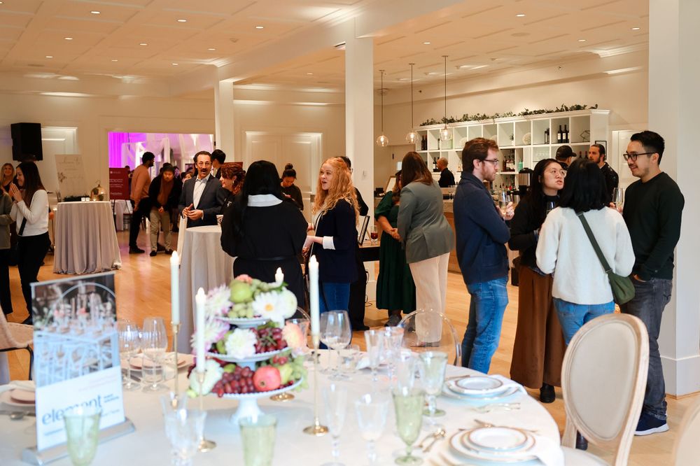 Evening event venue with decorated tables and mingling guests in a bright indoor space.