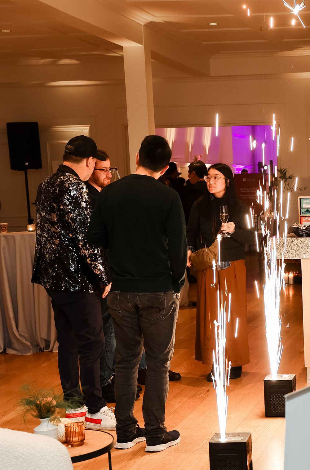 Event guests gathered around sparkler display in dimly lit venue space.