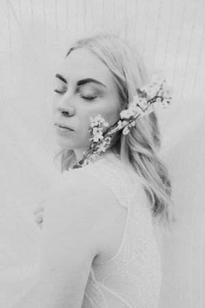 Ethereal black and white portrait of a woman with flowers in her hair against a light background.