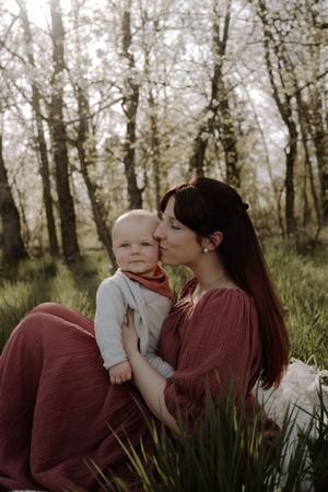 Mother and baby share tender moment in misty forest setting.