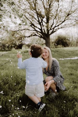 A tender springtime moment captured between a parent and child playing in a grassy field beneath a blooming tree.