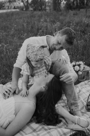 A black and white candid photo of a family enjoying a picnic on a blanket outdoors.