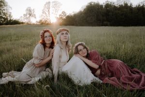 Three people in flowing dresses lounging in a sunset-lit meadow creating a bohemian atmosphere.
