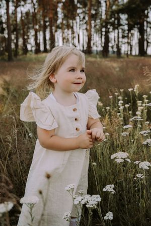 A dreamy portrait of a child in a white dress among wildflowers and tall grass.