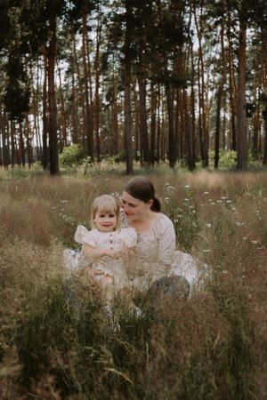 A tender outdoor portrait in a pine forest with soft lighting and wildflowers in the foreground.