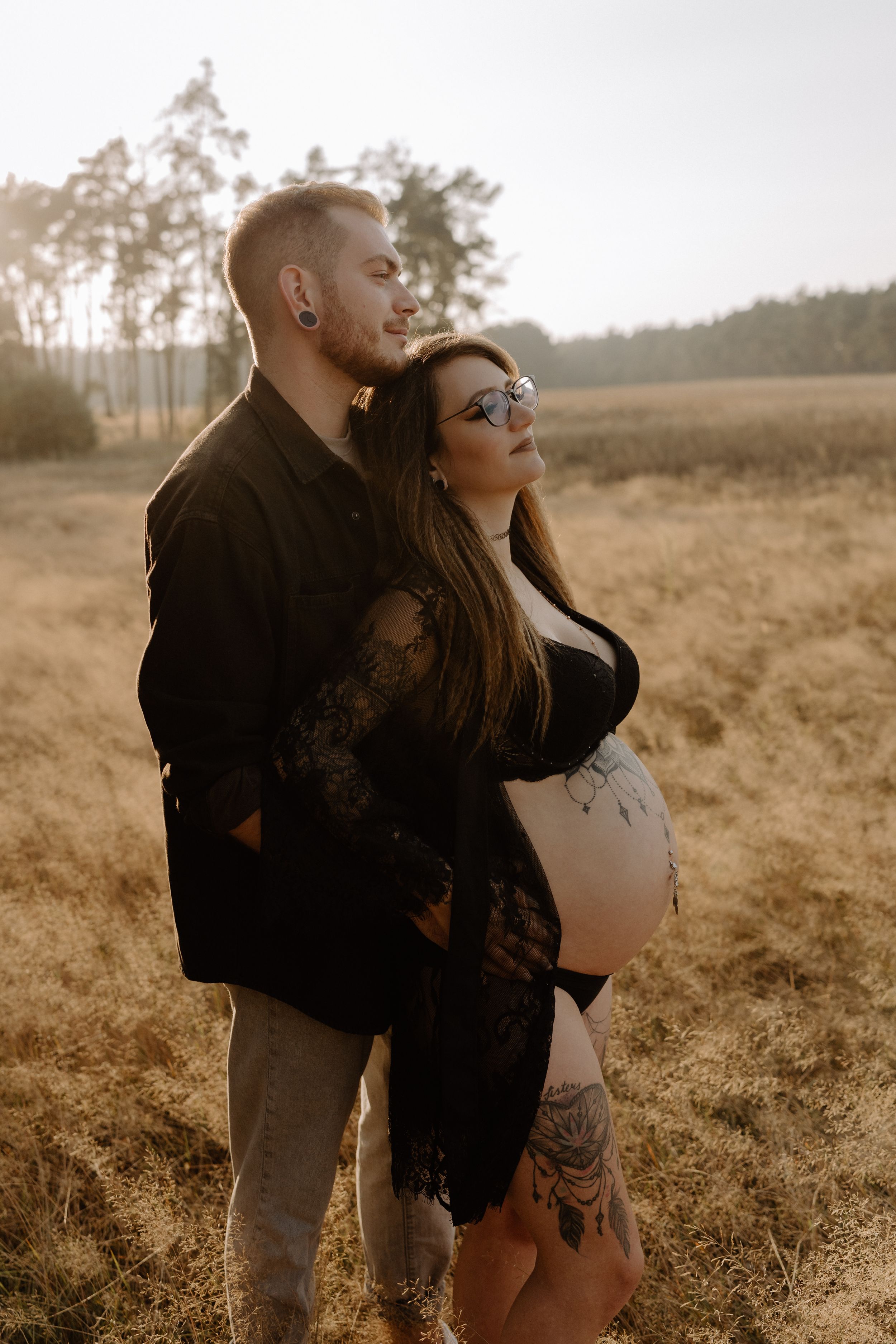 Romantic maternity photo of couple embracing in black attire during golden hour.