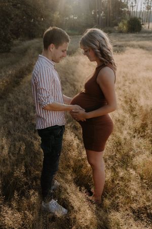 Intimate maternity moment captured in a sun-drenched field at golden hour.
