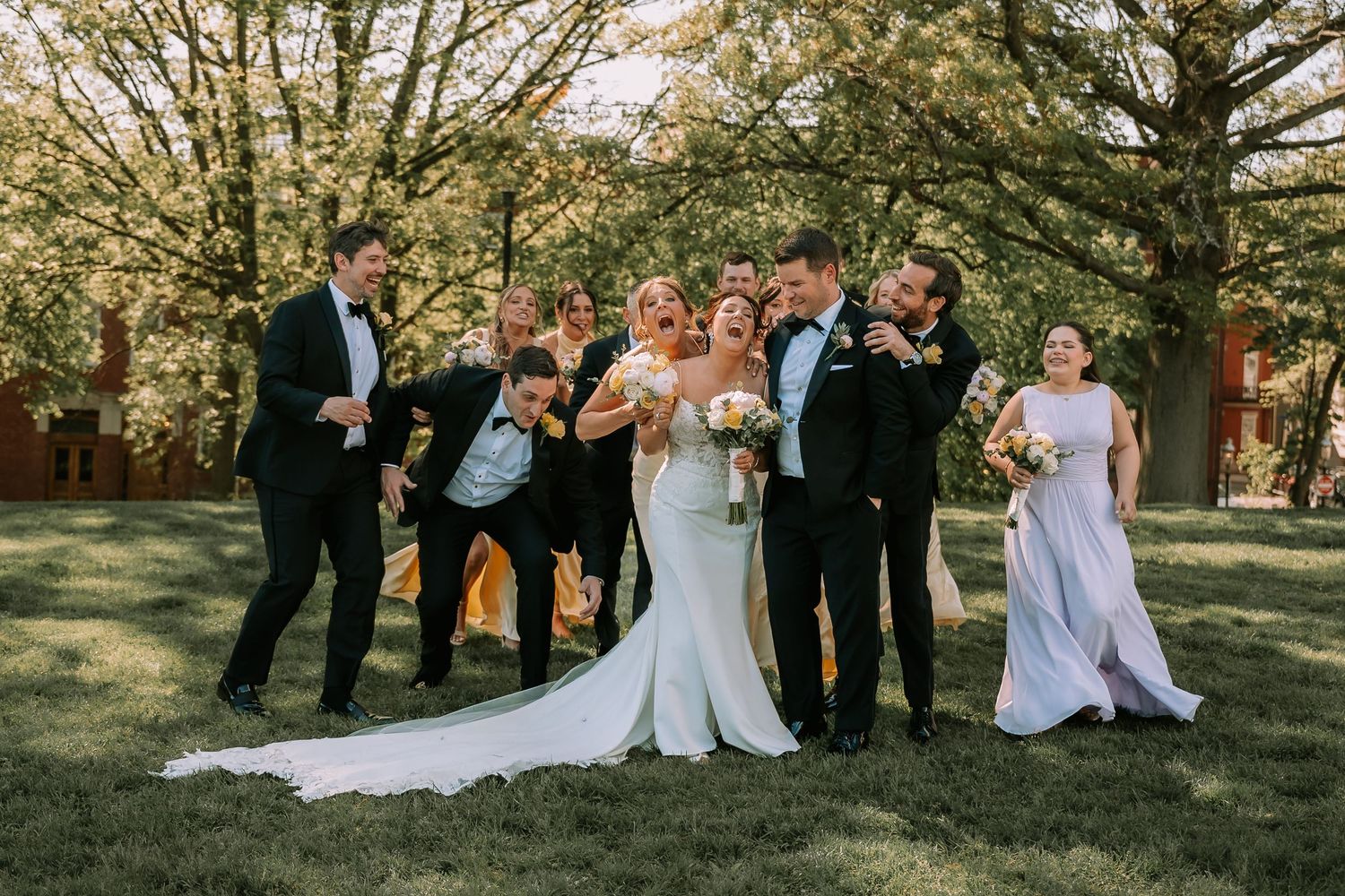 Wedding party celebrates outdoors under trees in formal attire.