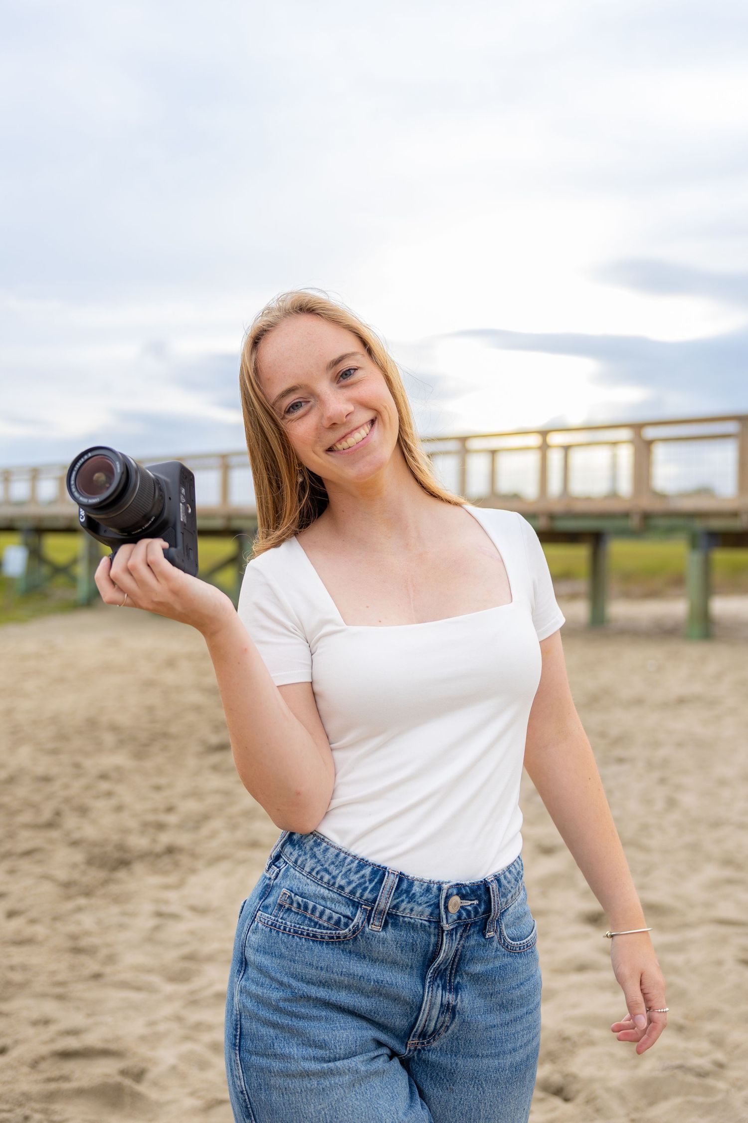 A photographer sits on sandy beach rocks at sunset holding a professional camera.