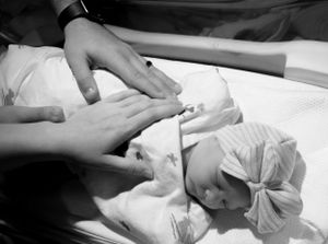 Black and white newborn photo of parents gently touching their sleeping baby in hospital.